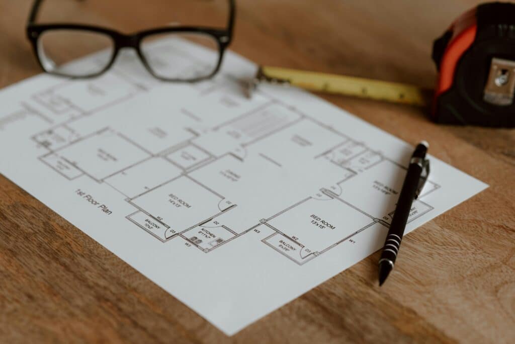 Floor plan with pen, glasses, and tape measure on a wooden desk