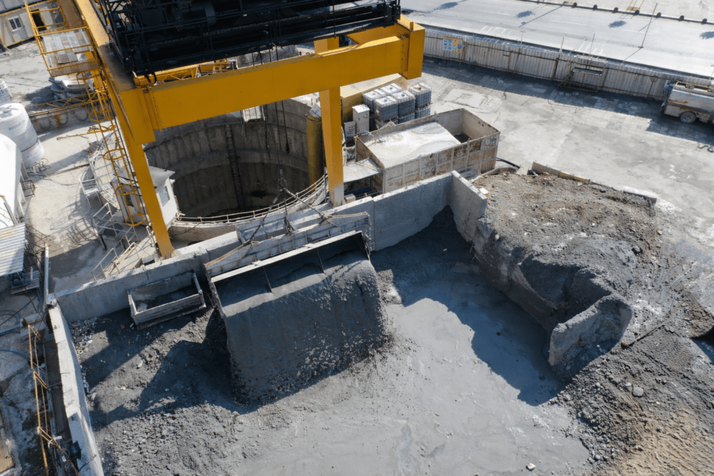 Aerial view of gantry crane operating over deep concrete excavation pit at industrial construction site