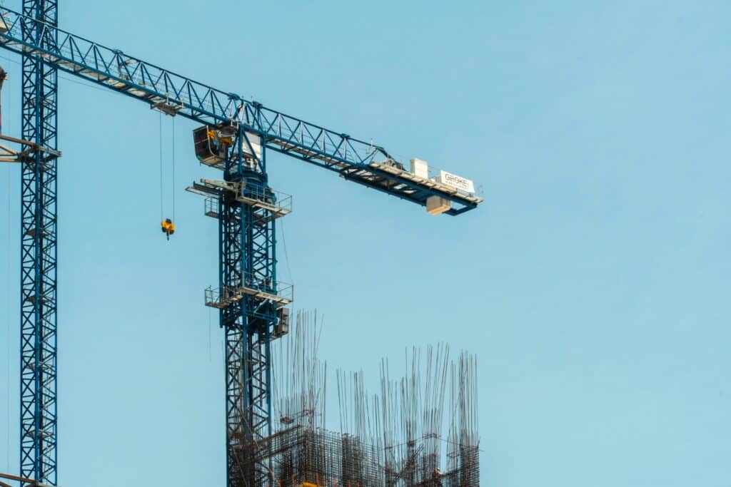 Construction site with exposed rebar columns and tall crane overhead.