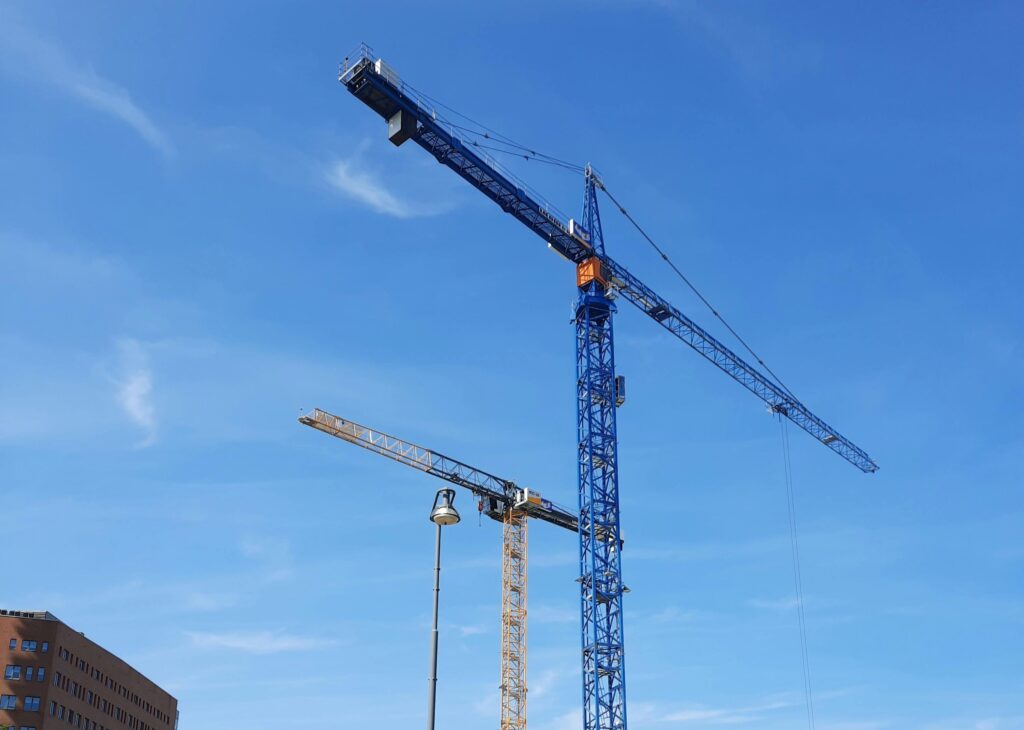 Tower cranes operating on a commercial construction site under a clear blue sky