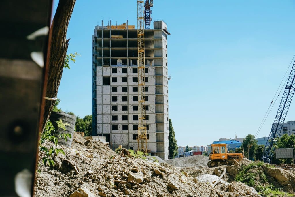 Concrete mid-rise building under construction with tower crane and bulldozer on an active urban job site under clear blue sky