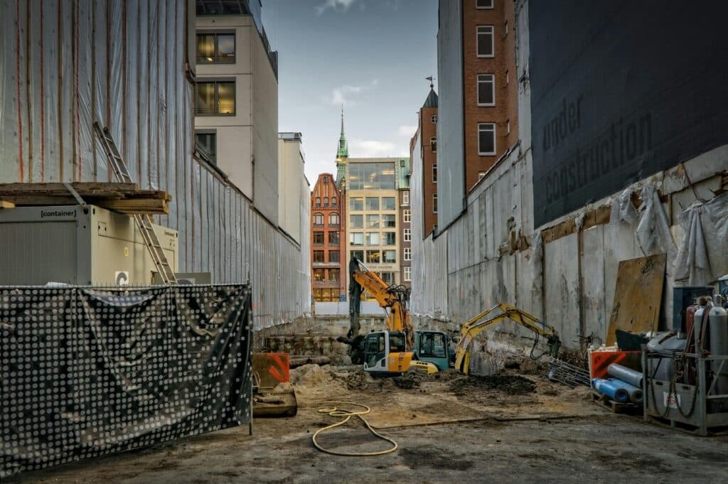 Excavators working at a narrow urban construction site surrounded by tall buildings in a city.