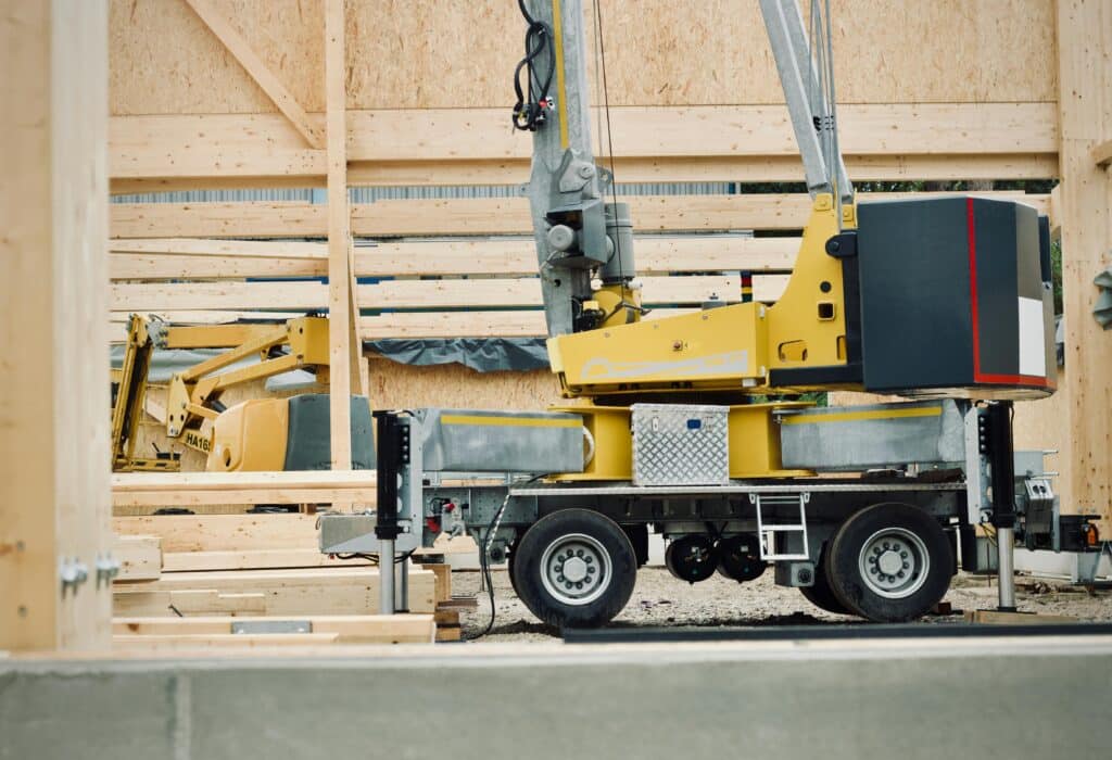 Trailer-mounted construction crane lifting wooden structural panels at a wood-frame building site.