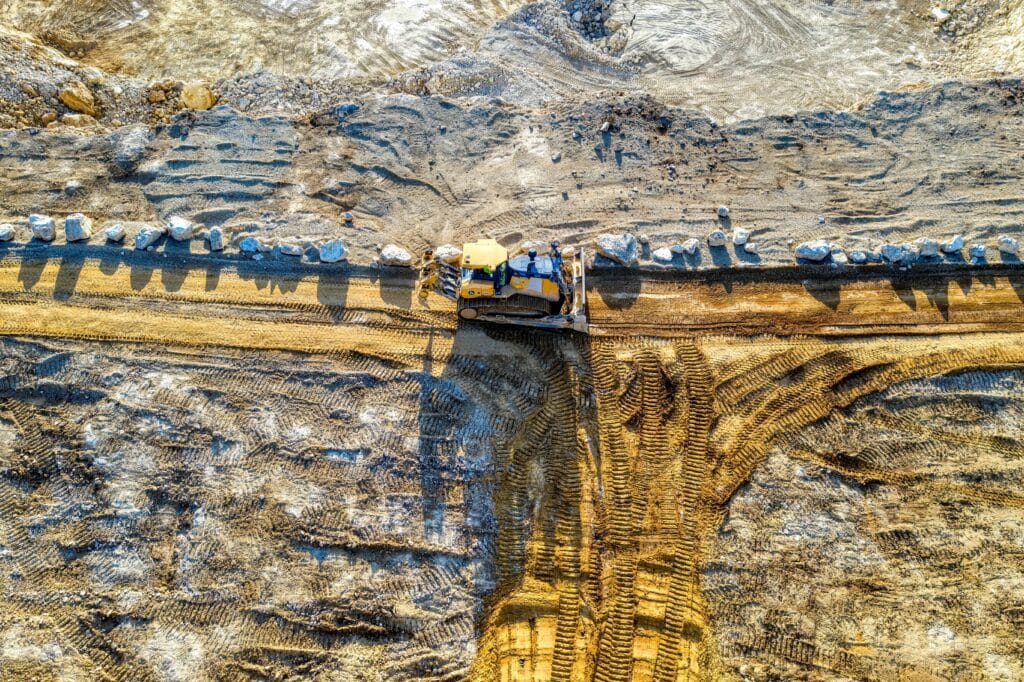 Top-down view of bulldozer leveling dirt road with visible tire tracks and rocks at construction site