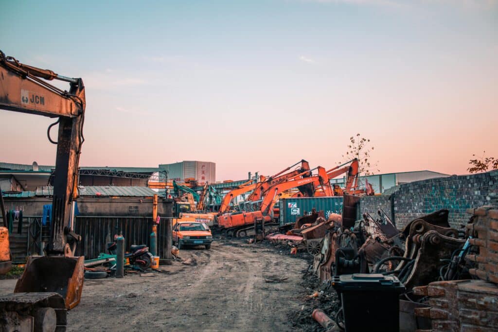 Excavators and demolition equipment in an industrial construction yard at sunset.