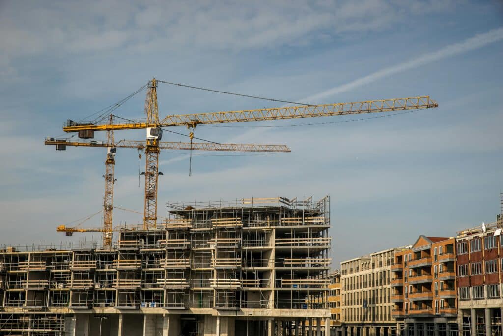 Tower cranes working over a multi-story building under construction in a modern urban area.