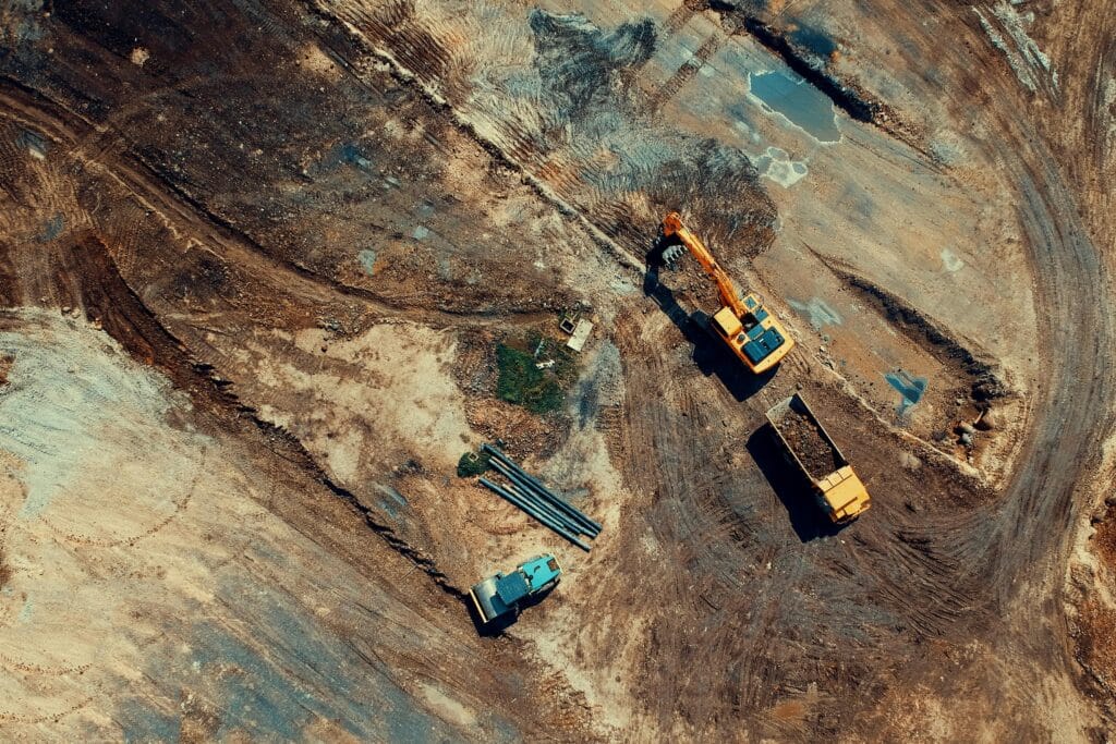 Top-down view of excavator loading soil into dump truck at large dirt construction site