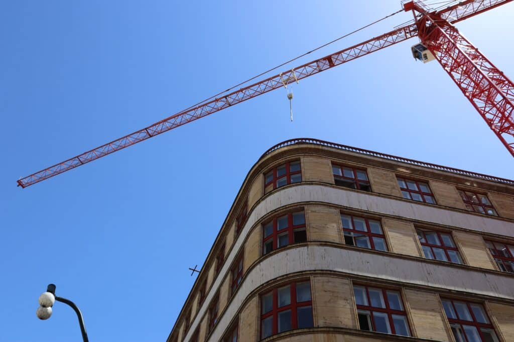 Red tower crane above multi-story commercial building under construction against a clear blue sky