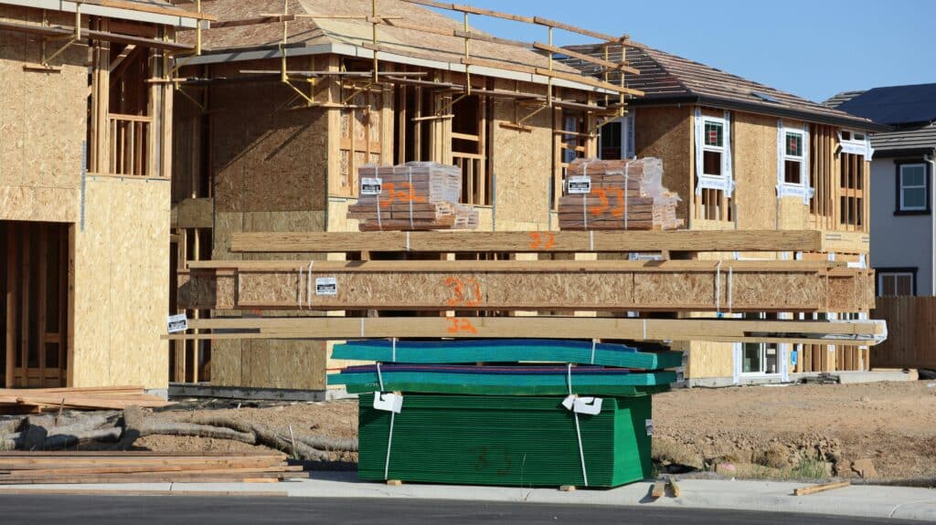 Wood-framed house under construction with stacked lumber and building materials at a residential job site