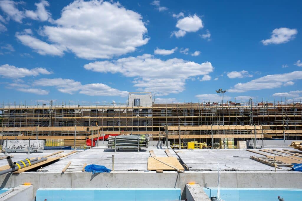 Multi-story commercial building under construction with scaffolding and materials on site under a blue sky