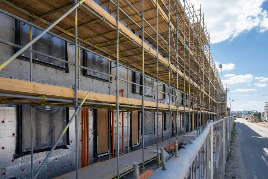Scaffolding installed along a large commercial building under construction with exterior insulation and window openings visible