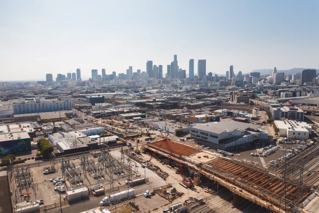 Aerial view of a large commercial construction site with bridge work, industrial infrastructure, and a city skyline, showcasing skilled trades workforce solutions for modern construction projects.